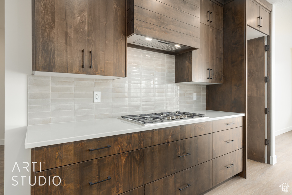 Kitchen with premium range hood, tasteful backsplash, dark brown cabinetry, and light wood-type flooring