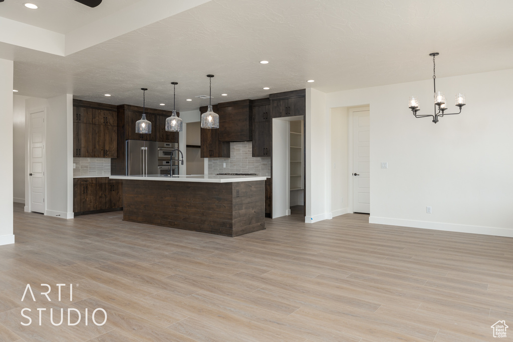 Kitchen featuring stainless steel appliances, a notable chandelier, tasteful backsplash, a center island with sink, and light hardwood / wood-style flooring