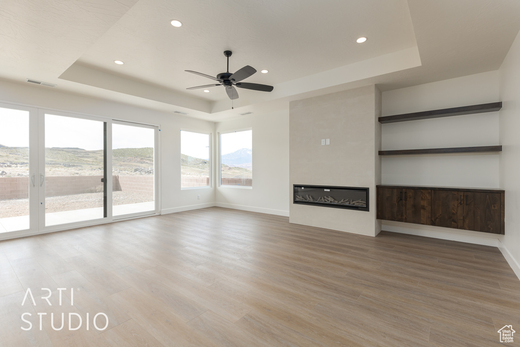 Unfurnished living room featuring light hardwood / wood-style floors, a tray ceiling, and ceiling fan