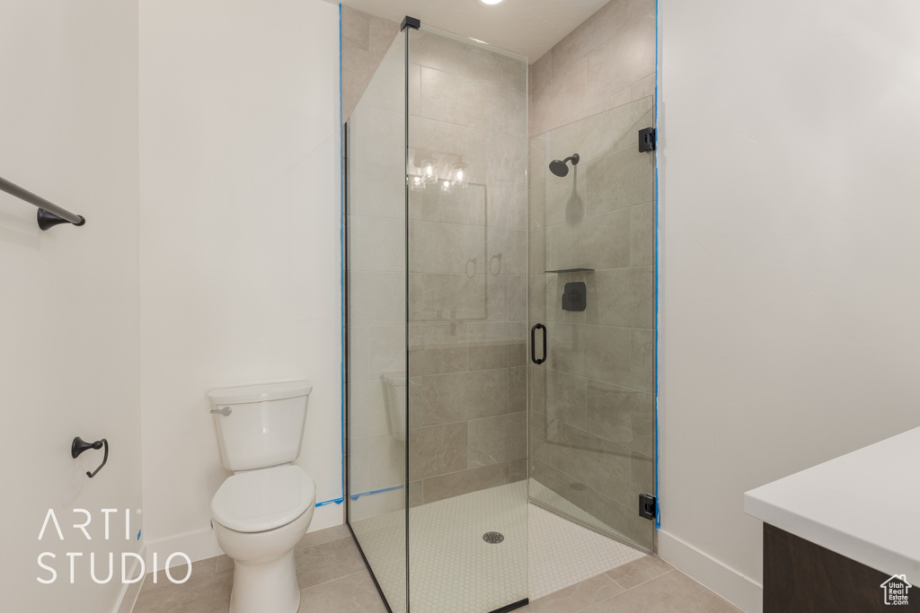 Bathroom with toilet, a shower with door, tile floors, and vanity