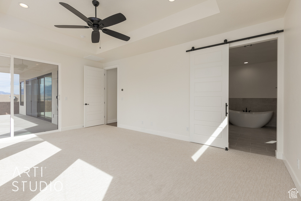 Carpeted spare room featuring a barn door and ceiling fan