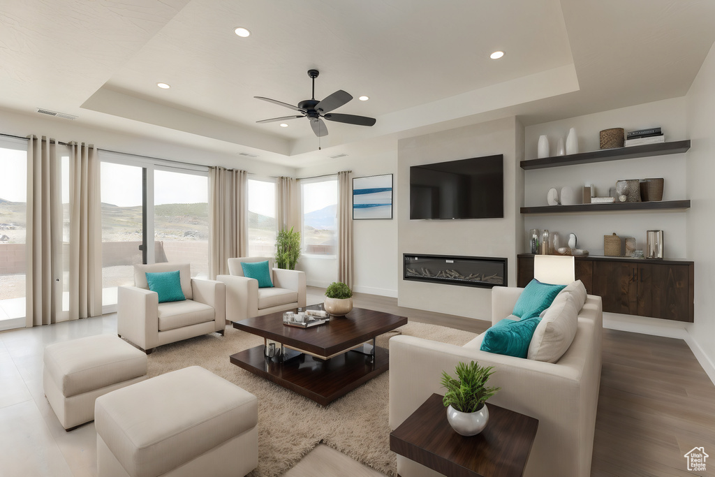 Living room with ceiling fan, a raised ceiling, and light hardwood / wood-style flooring