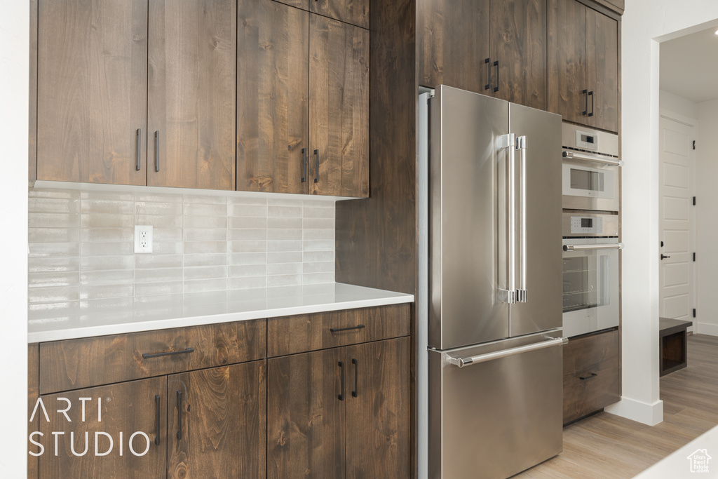 Kitchen with backsplash, high end refrigerator, light hardwood / wood-style flooring, double wall oven, and dark brown cabinets