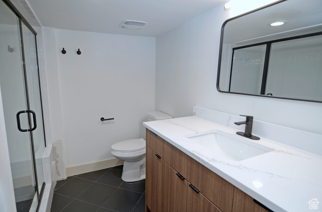 Bathroom featuring an enclosed shower, vanity, tile flooring, and toilet