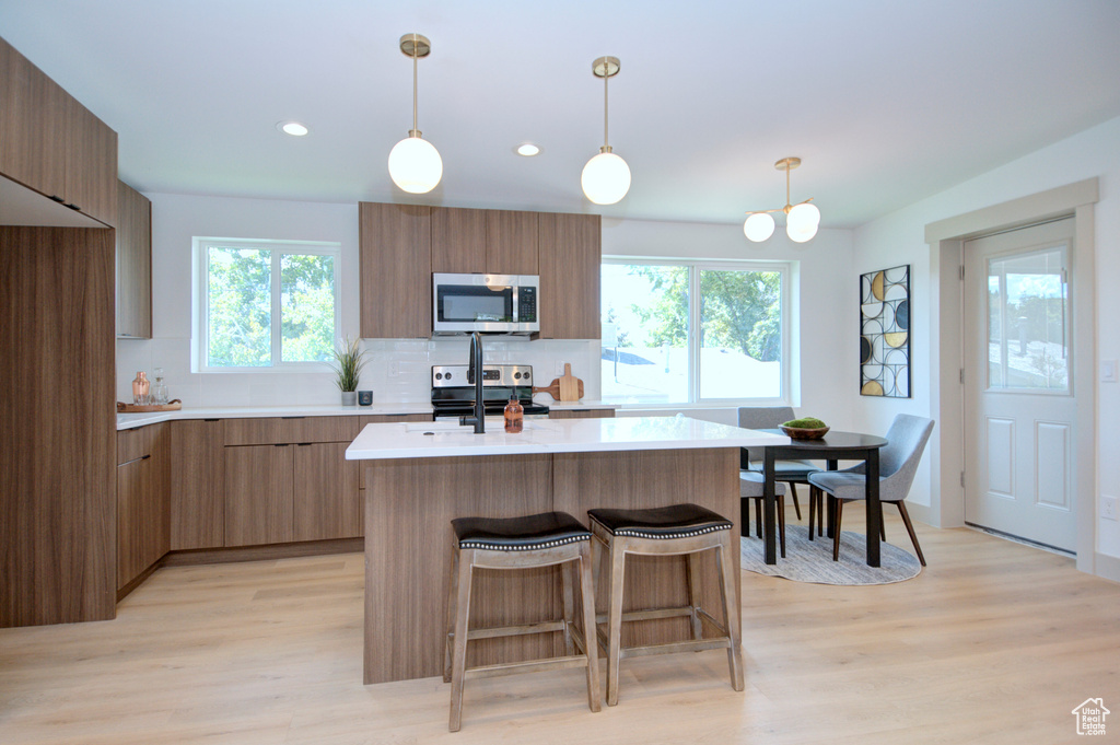 Kitchen featuring an inviting chandelier, tasteful backsplash, hanging light fixtures, appliances with stainless steel finishes, and light hardwood / wood-style flooring