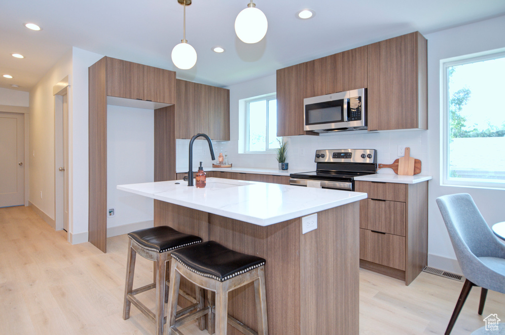 Kitchen featuring light hardwood / wood-style flooring, an island with sink, stainless steel appliances, and decorative light fixtures