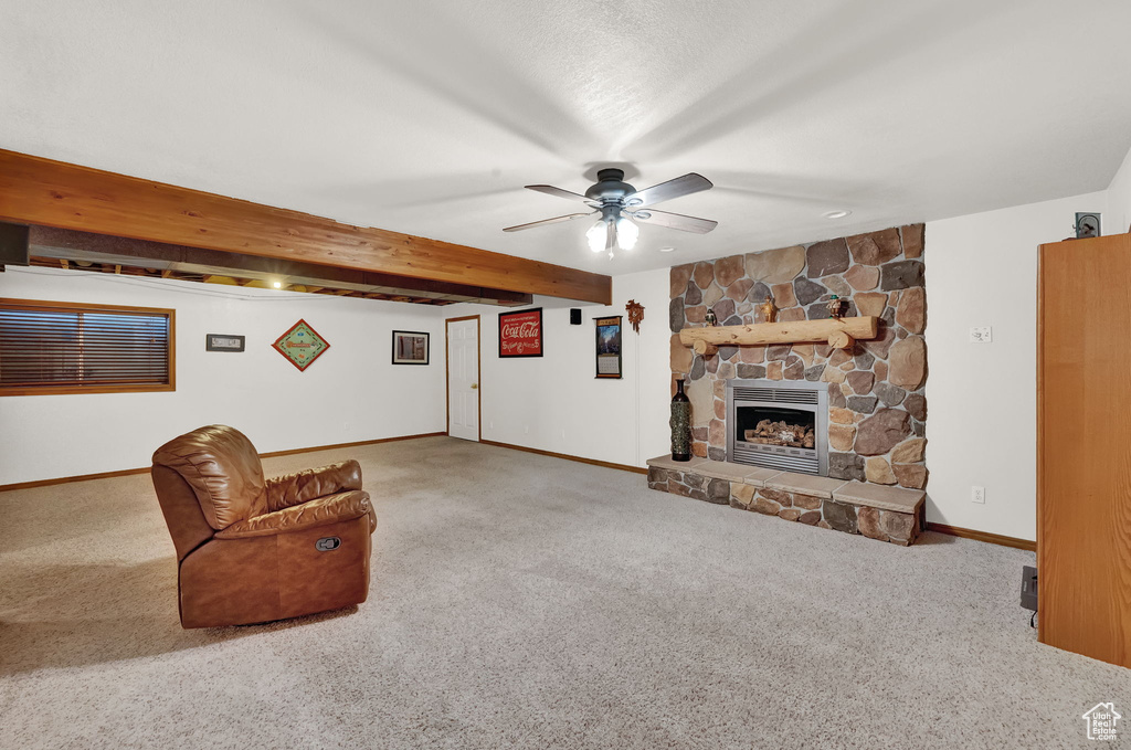 Carpeted living room featuring a stone fireplace, beamed ceiling, and ceiling fan