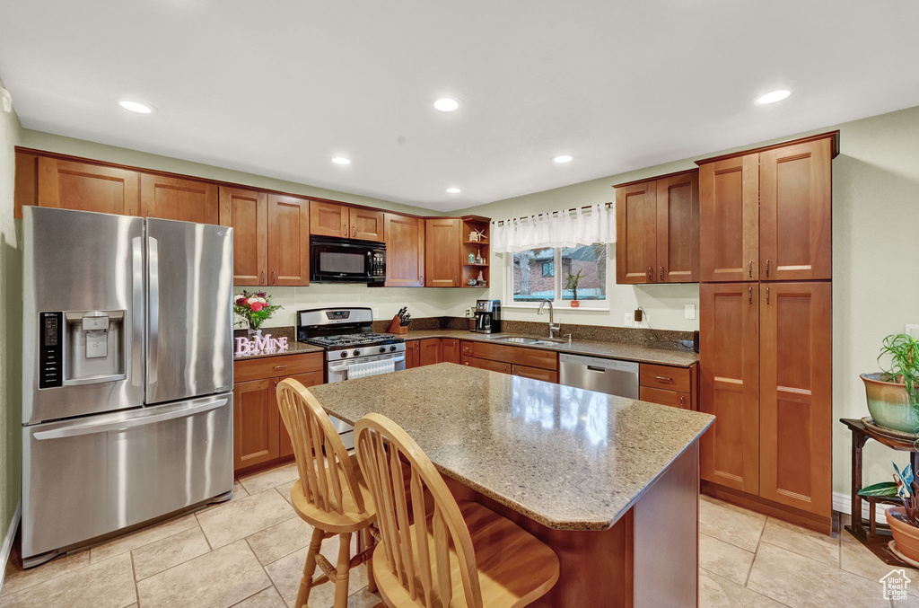 Kitchen featuring light tile flooring, appliances with stainless steel finishes, a center island, and a breakfast bar area