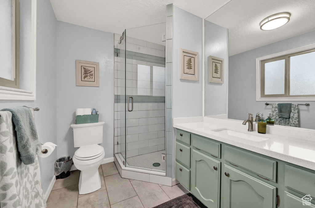 Bathroom with a textured ceiling, toilet, a shower with door, tile floors, and vanity with extensive cabinet space