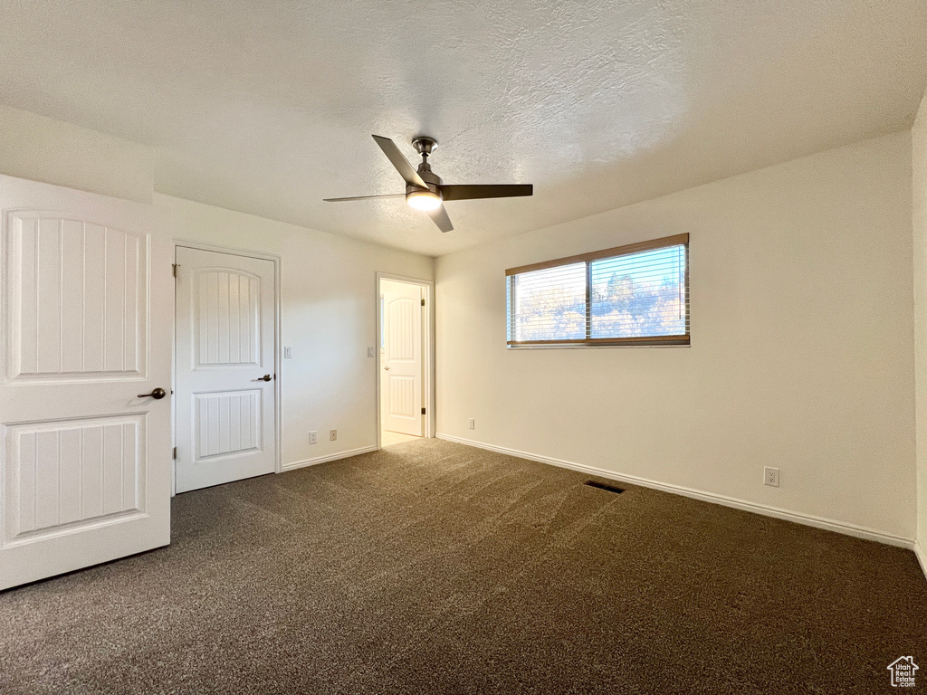 Unfurnished bedroom featuring dark colored carpet and ceiling fan