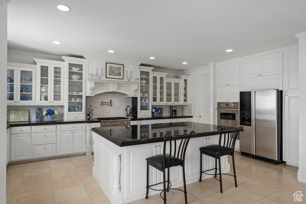 Kitchen featuring backsplash, a breakfast bar area, white cabinetry, premium range hood, and appliances with stainless steel finishes