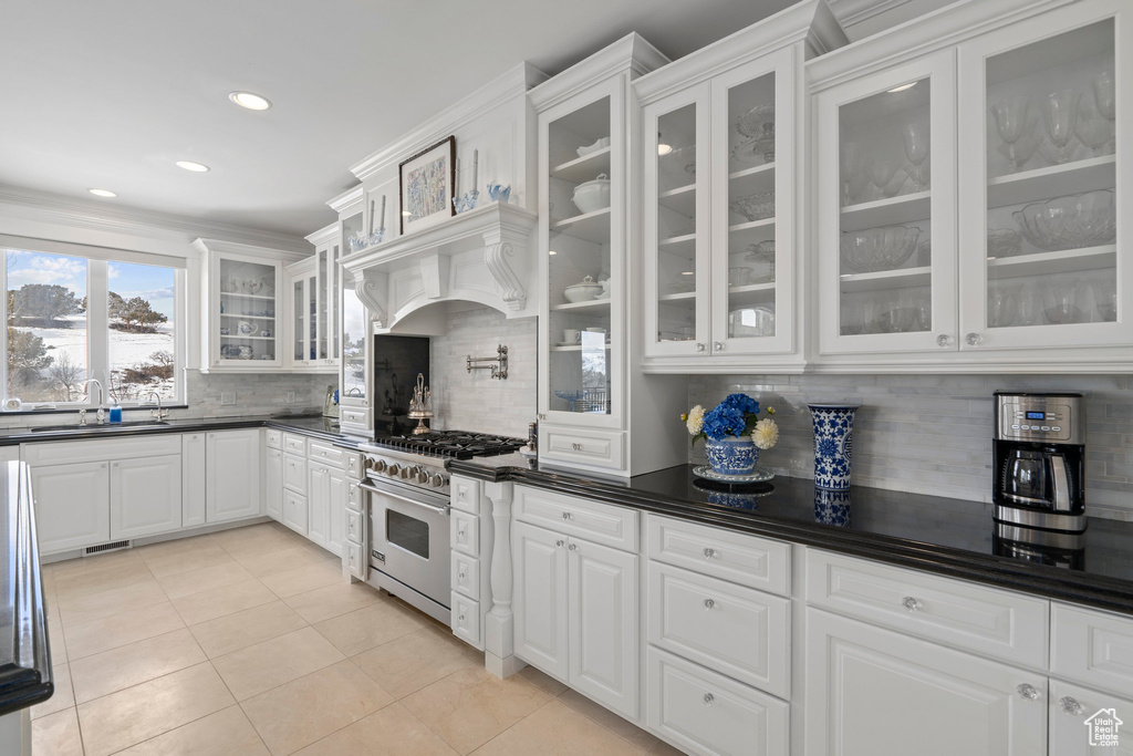 Kitchen with high end range, white cabinetry, backsplash, sink, and light tile floors