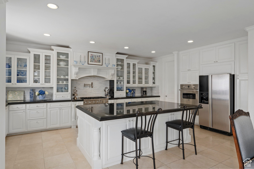 Kitchen with a kitchen breakfast bar, white cabinetry, tasteful backsplash, light tile floors, and stainless steel appliances