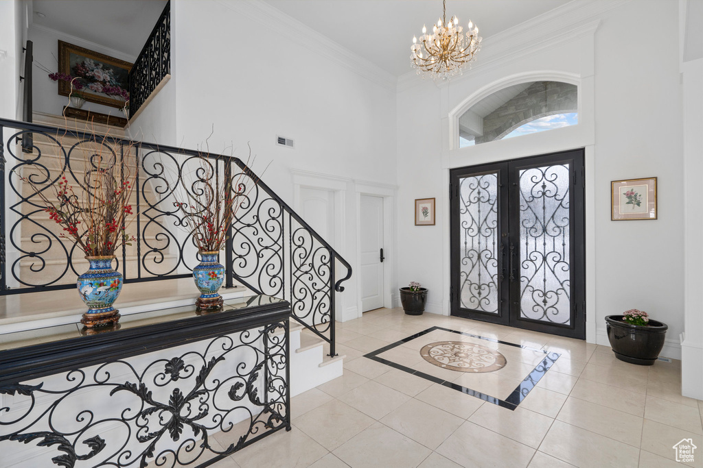 Foyer with crown molding, a high ceiling, french doors, a chandelier, and light tile flooring