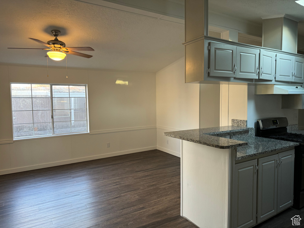 Kitchen featuring stove, ceiling fan, dark hardwood / wood-style flooring, dark stone countertops, and kitchen peninsula