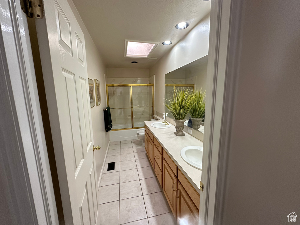 Full bathroom featuring double sink, combined bath / shower with glass door, large vanity, toilet, and a skylight