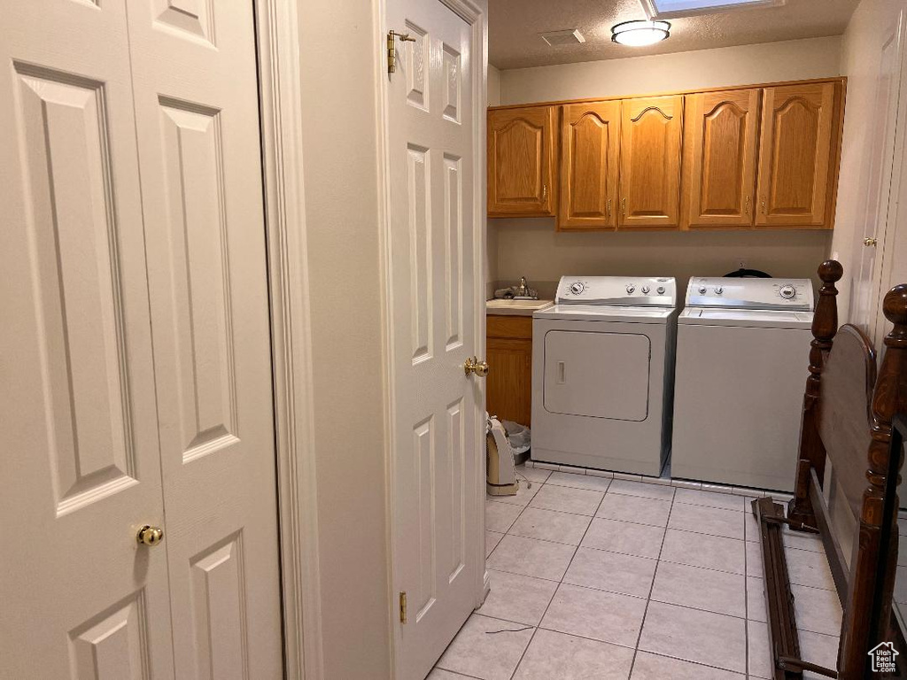 Clothes washing area with light tile floors, washer and dryer, sink, and cabinets