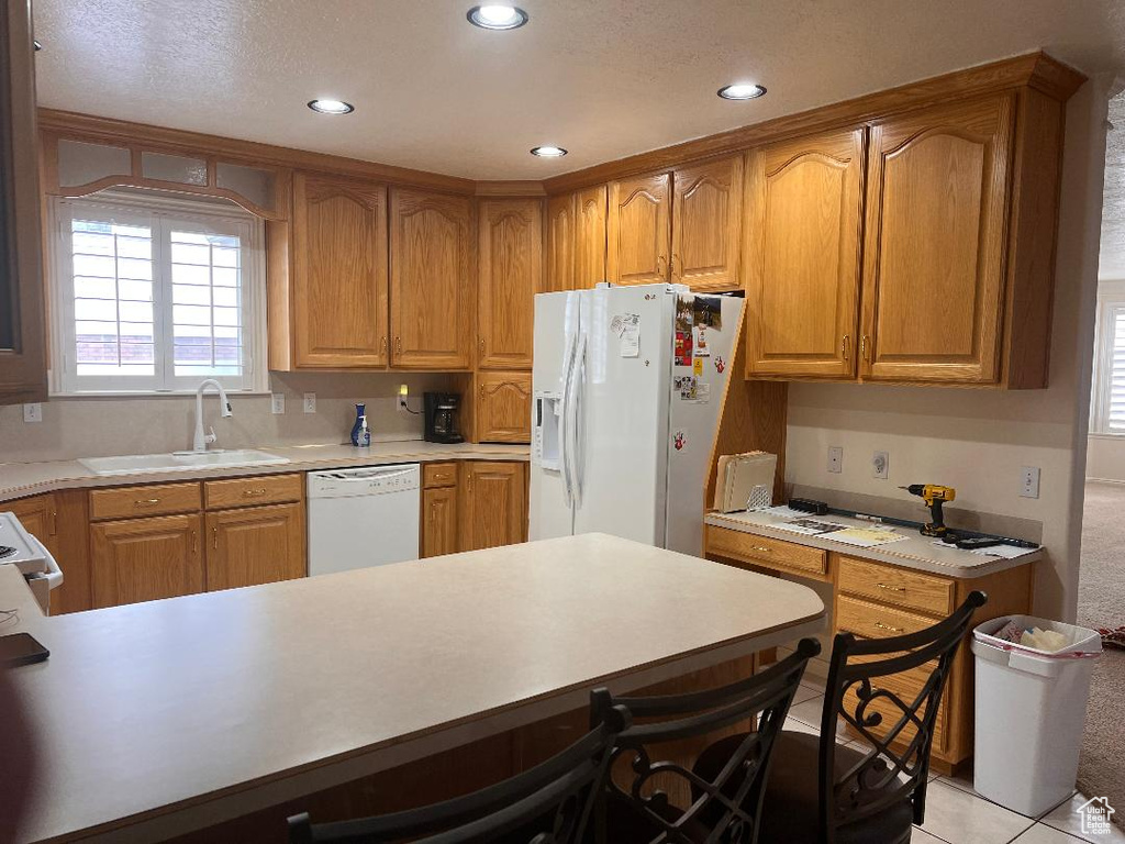 Kitchen featuring white appliances, a breakfast bar, light tile floors, and sink