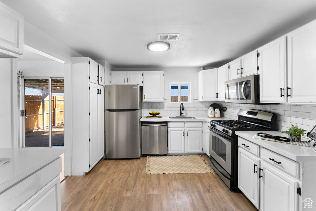 Kitchen featuring light wood-type flooring, appliances with stainless steel finishes, backsplash, and white cabinets