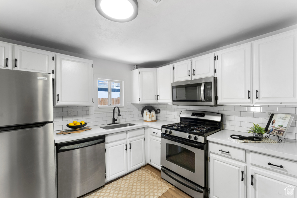 Kitchen with white cabinets, stainless steel appliances, backsplash, and sink