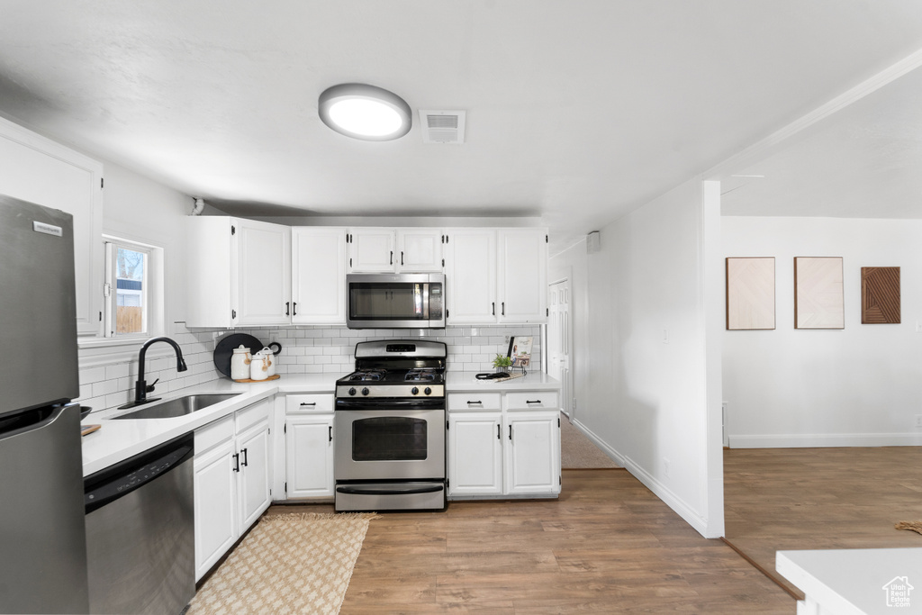 Kitchen featuring light wood-type flooring, white cabinetry, stainless steel appliances, and sink