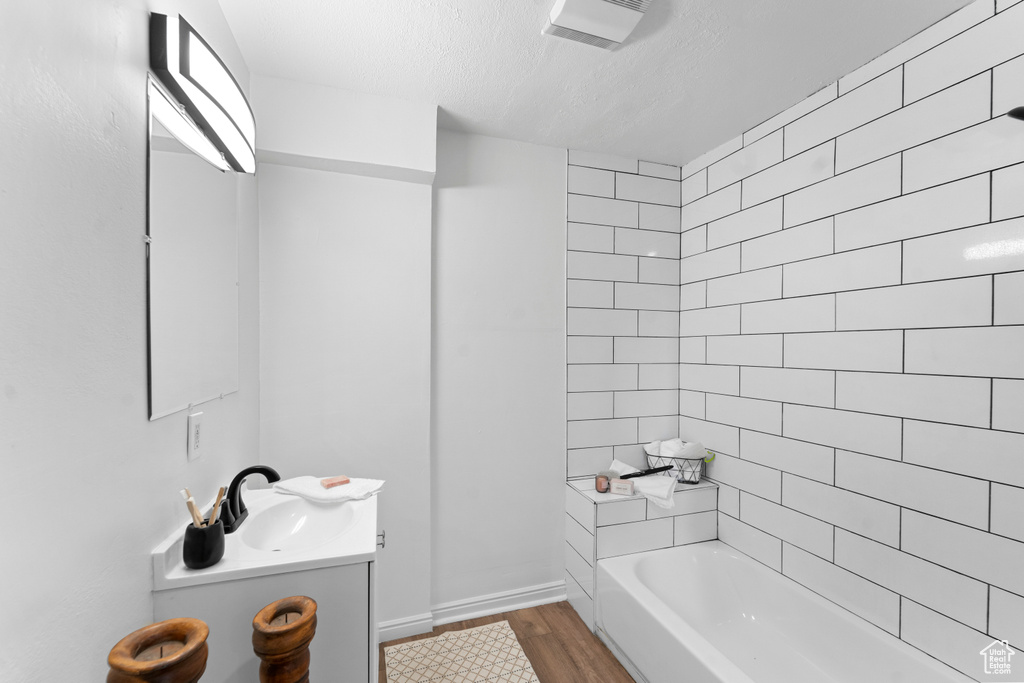 Bathroom with hardwood / wood-style floors, tiled shower / bath, vanity, and a textured ceiling