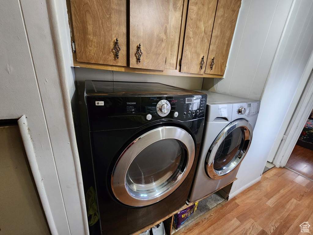 Clothes washing area with cabinets, light hardwood / wood-style floors, and separate washer and dryer