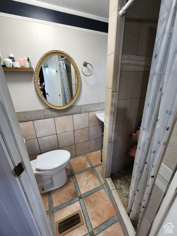 Bathroom featuring a shower with curtain, tile walls, tile flooring, and toilet