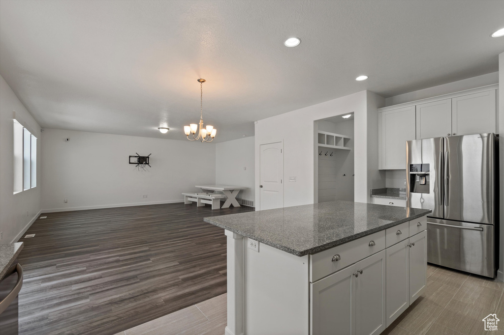 Kitchen featuring stainless steel refrigerator with ice dispenser, white cabinets, a center island, an inviting chandelier, and hardwood / wood-style flooring