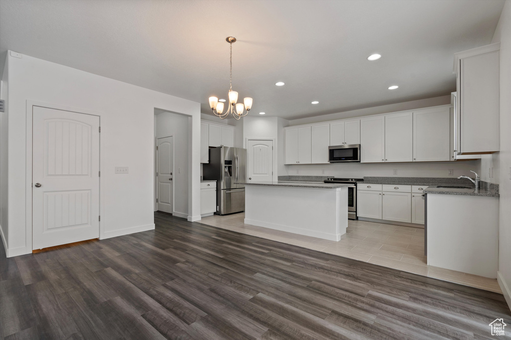 Kitchen with a chandelier, appliances with stainless steel finishes, a kitchen island, and wood-type flooring