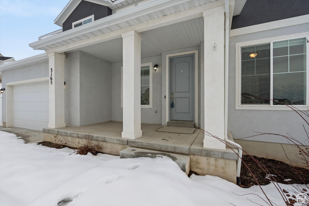 Snow covered property entrance with a garage and covered porch