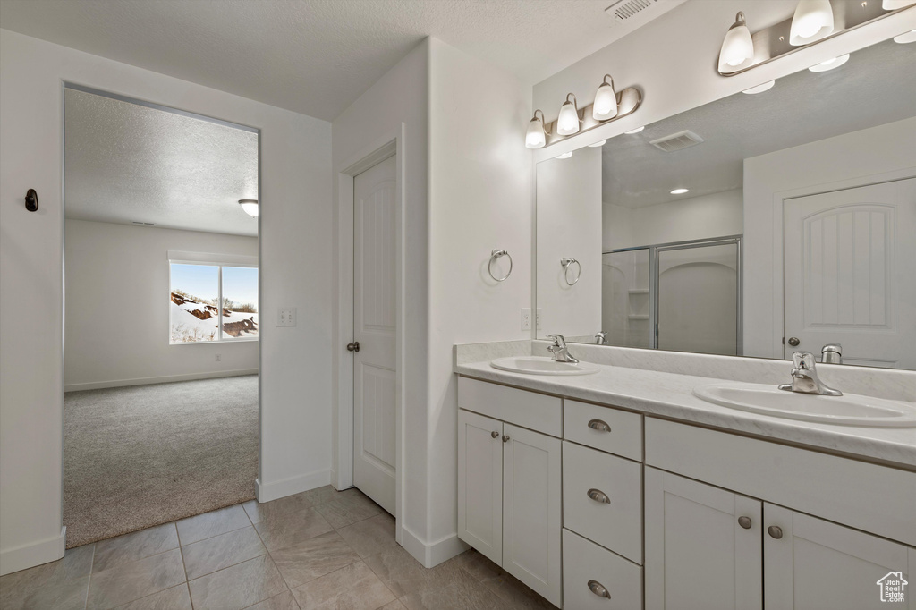 Bathroom with large vanity, dual sinks, tile floors, and a textured ceiling