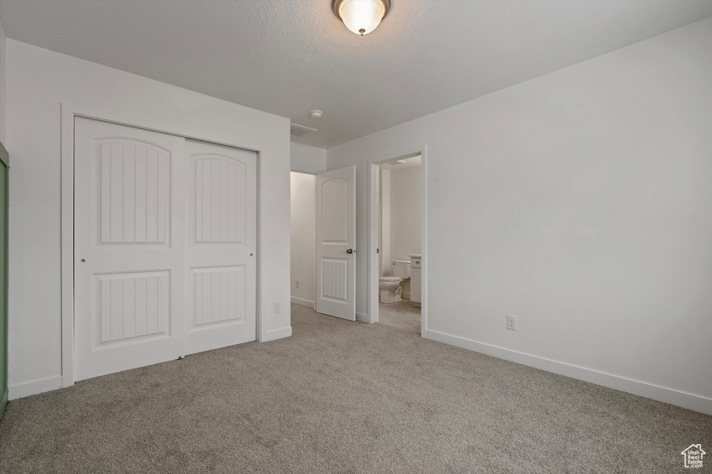 Unfurnished bedroom featuring light colored carpet, ensuite bathroom, and a closet