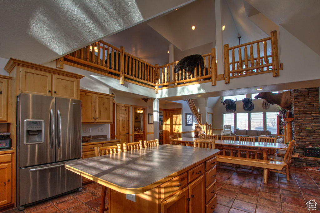 Kitchen with a kitchen island, a high ceiling, dark tile flooring, and stainless steel fridge