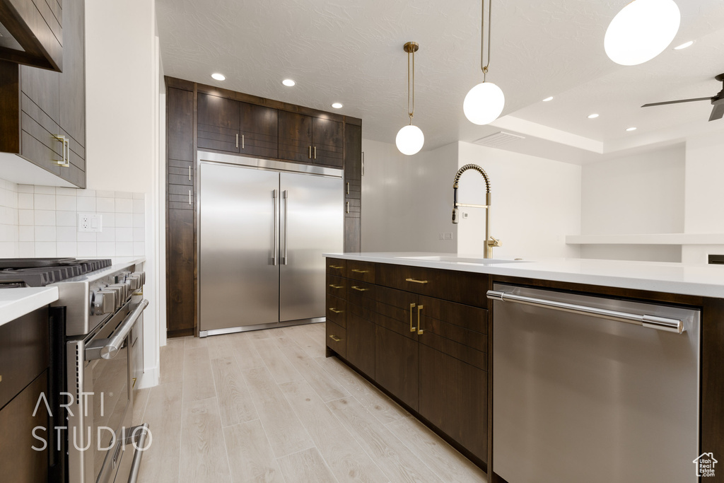 Kitchen featuring dark brown cabinetry, sink, premium appliances, decorative light fixtures, and light hardwood / wood-style floors