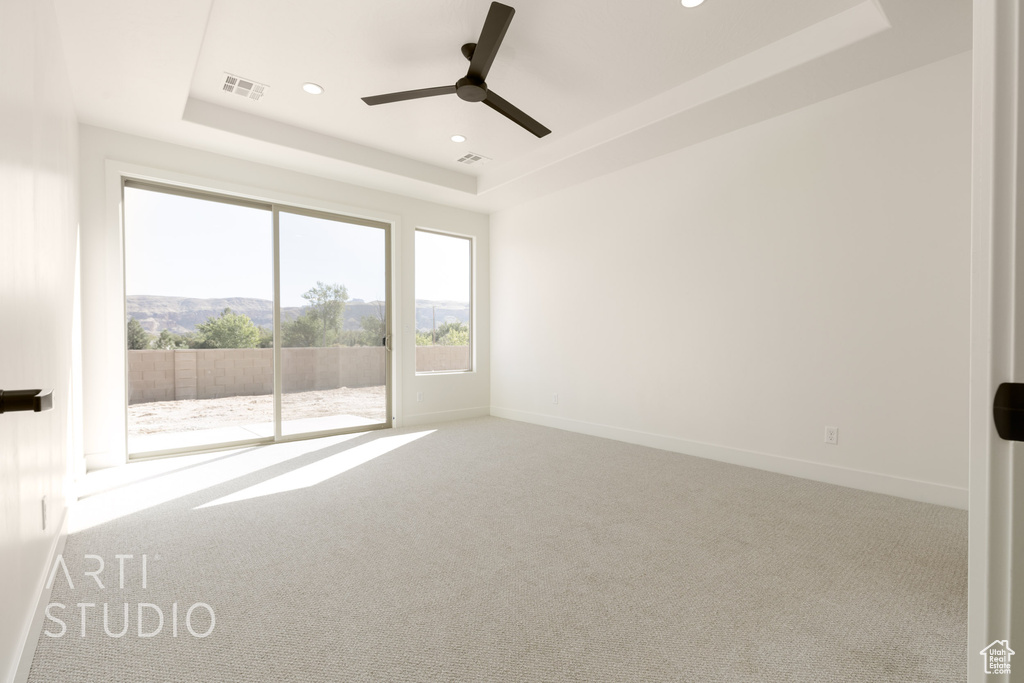 Carpeted spare room featuring a raised ceiling and ceiling fan