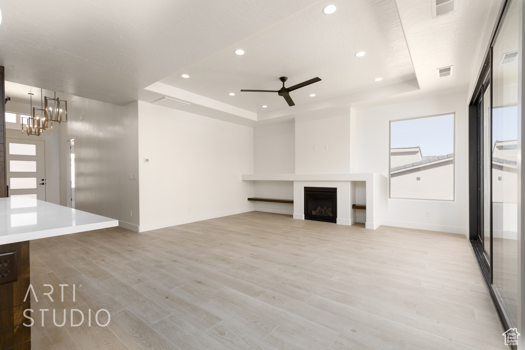 Unfurnished living room with ceiling fan with notable chandelier, a raised ceiling, and light hardwood / wood-style floors