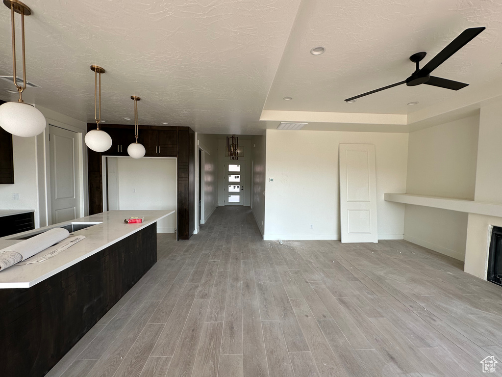 Kitchen with dark brown cabinets, decorative light fixtures, light wood-type flooring, ceiling fan, and a raised ceiling