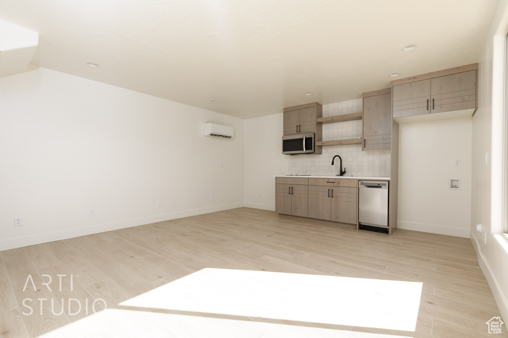 Kitchen with a wall mounted air conditioner, sink, tasteful backsplash, appliances with stainless steel finishes, and light hardwood / wood-style floors