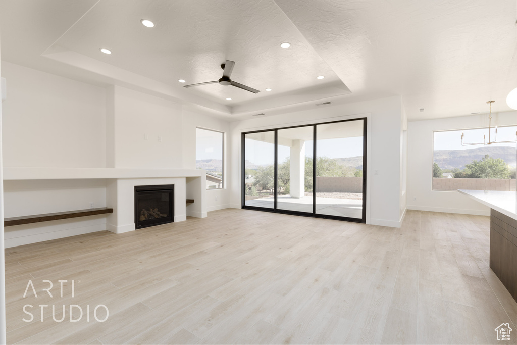 Unfurnished living room with ceiling fan, a raised ceiling, and light hardwood / wood-style floors