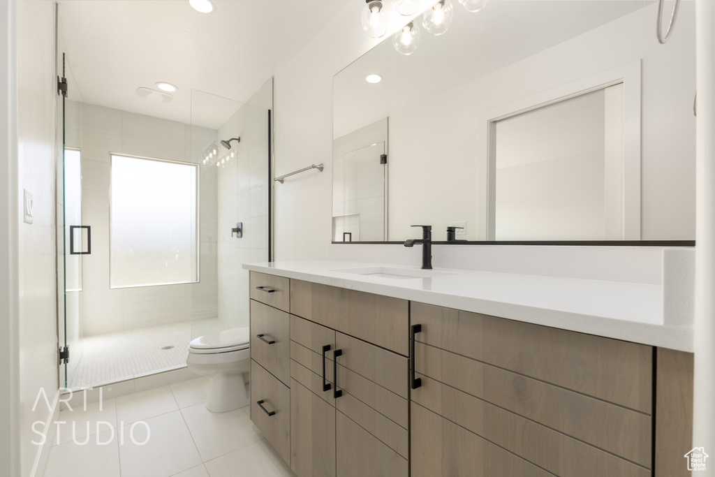 Bathroom with tiled shower, tile patterned floors, vanity, and toilet