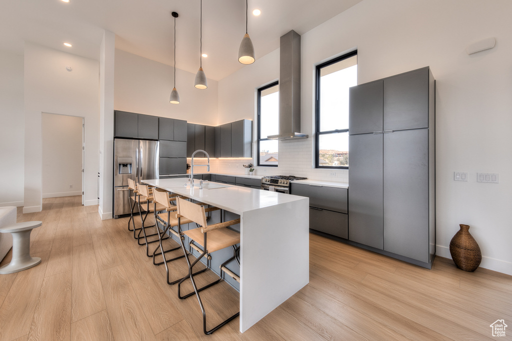 Kitchen featuring pendant lighting, a breakfast bar, wall chimney exhaust hood, light wood-type flooring, and appliances with stainless steel finishes