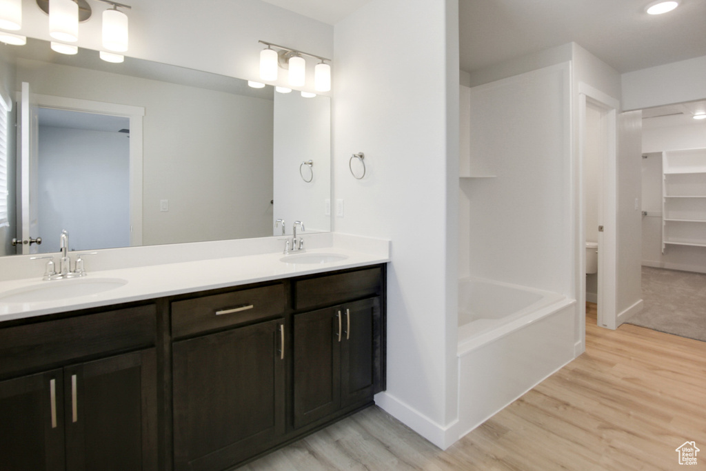 Full bathroom with hardwood / wood-style floors, large vanity, toilet, tub / shower combination, and dual sinks