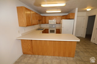 Kitchen with white appliances, sink, light tile flooring, and kitchen peninsula