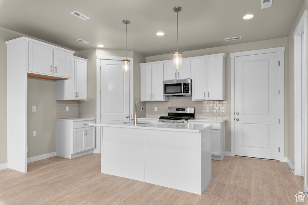 Kitchen with stainless steel appliances, white cabinetry, light wood-type flooring, and an island with sink