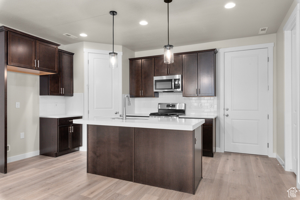 Kitchen with hanging light fixtures, light hardwood / wood-style flooring, range with gas cooktop, a center island with sink, and sink