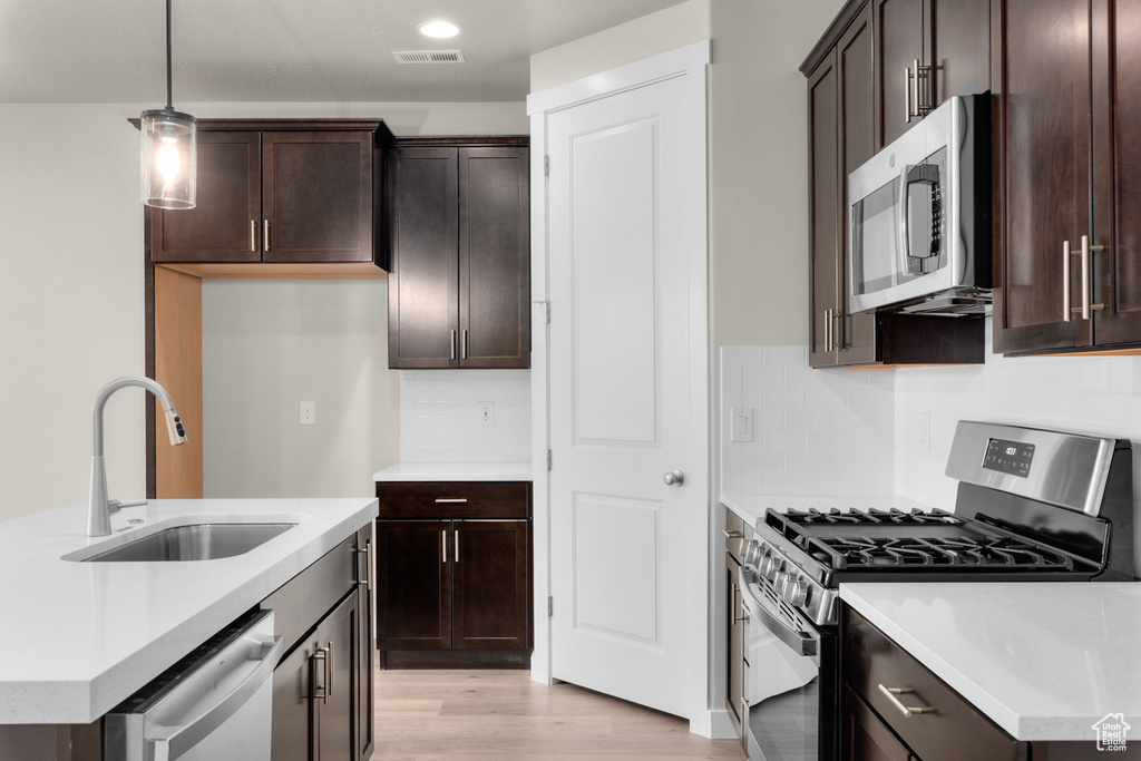 Kitchen featuring light hardwood / wood-style floors, pendant lighting, tasteful backsplash, appliances with stainless steel finishes, and sink