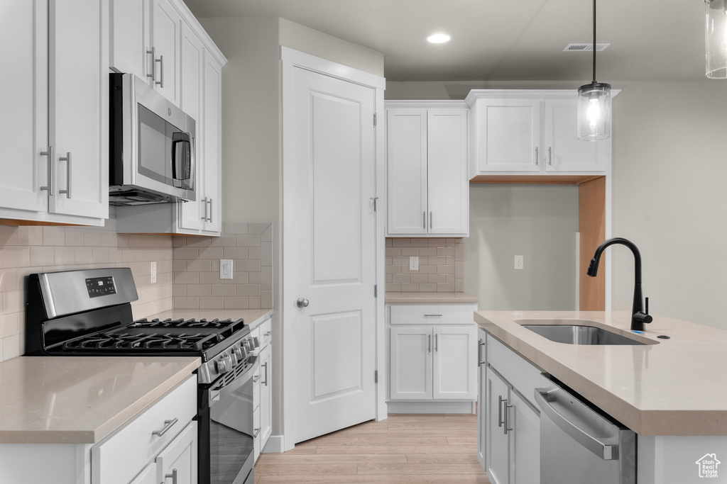 Kitchen with light wood-type flooring, white cabinets, hanging light fixtures, sink, and appliances with stainless steel finishes