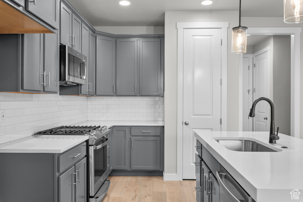 Kitchen with gray cabinets, light hardwood / wood-style flooring, appliances with stainless steel finishes, hanging light fixtures, and sink