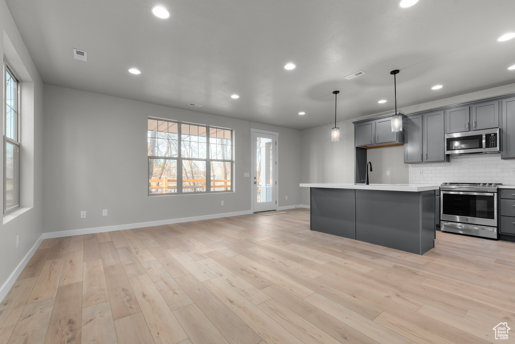 Kitchen with appliances with stainless steel finishes, pendant lighting, light wood-type flooring, and backsplash